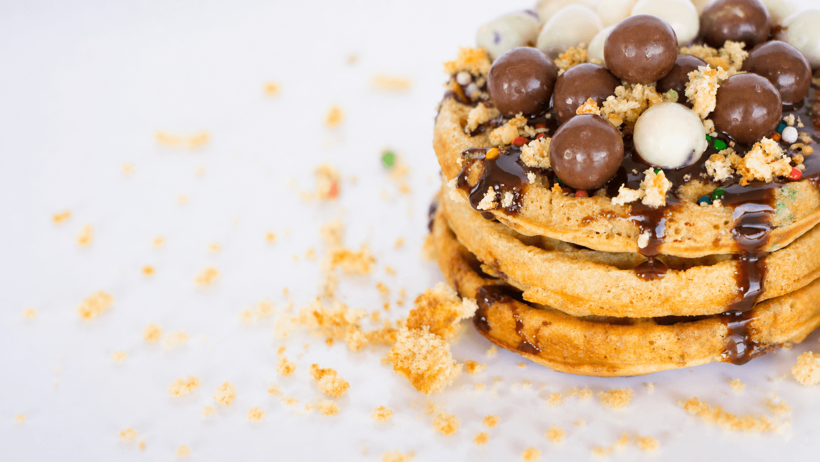 Waffles sabor birthday cake con chispas de colores, perlas de chocolate y salsa de chocolate encima
